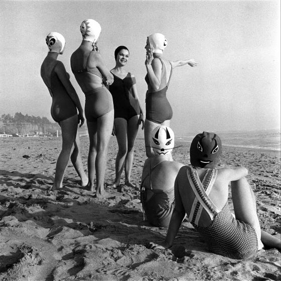 Women modeling bathing caps with faces on them.